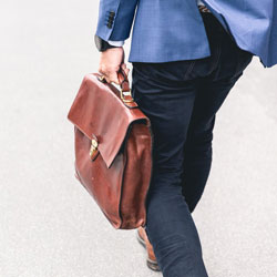A person walking with a briefcase. Photo Credit: Marten Bjork on Unsplash [https://unsplash.com/photos/6dW3xyQvcYE]