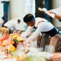 A waiter setting a table. Photo Credit: CHUTTERSNAP on Unsplash [https://unsplash.com/photos/OB7ol699Iww]