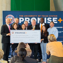 A group of University officials and students standing in front of a sign that reads “Promise Plus” while collectively holding a giant check for one million five hundred thousand dollars.