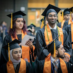 Four UT Dallas graduates in caps and gowns.