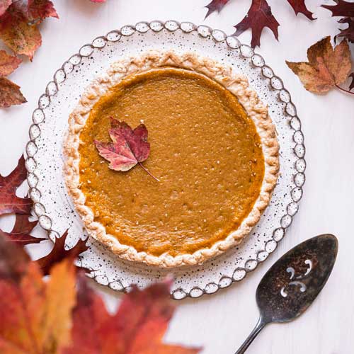 A pumkin pie, ready to be served. Photo Credit: Prchi Palwe on Unsplash [https://unsplash.com/photos/a-pie-sitting-on-top-of-a-white-table-next-to-leaves-V91vISyxD18]