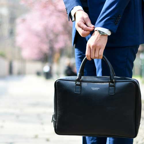 A person holding a briefcase while straightening a jacket cuff. Photo Credit: Andrea Natali on Unsplash [https://unsplash.com/photos/man-in-blue-suit-standing-on-street-side-while-holding-bag-during-daytime-jdTtkmr1axk]