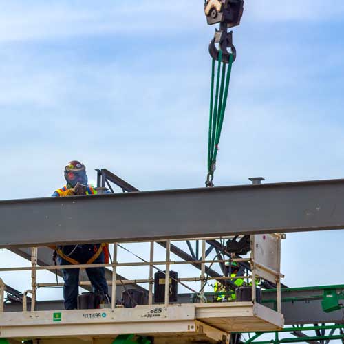 DFW Labor Market Update. A construction worker welds two roof beams together.