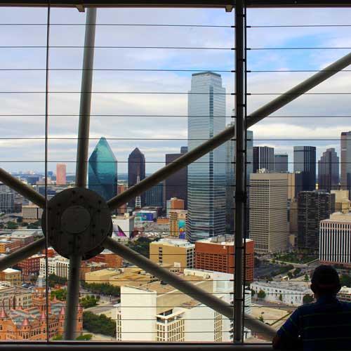 The Dallas skyline as seen from the observation deck of Reunion Tower. Photo Credit: CC0 1.0 2014 IcedCowboyCoffee [https://commons.wikimedia.org/wiki/File:Man_looks_out_at_the_Dallas_skyline_from_Reunion_Tower.png]