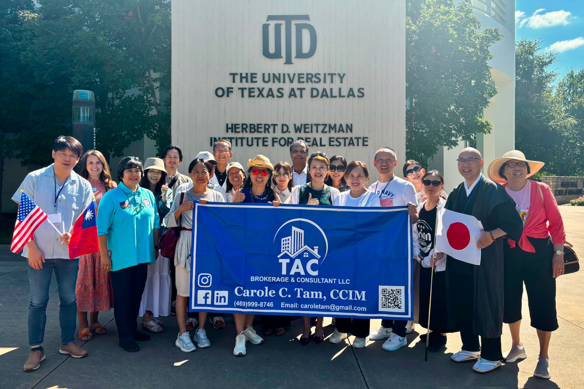 A group of people pose for a photo on the UT Dallas campus in front of a sign that reads “UTD, The University of Texas at Dallas, Herbert D. Weitzman Institute for Real Estate”. Among the group are people who hold the flags of the US, Taiwan, and Japan, as well as a banner that reads “TAC Brokerage and Consultant LLC, Carole C. Tam, CCIM”.